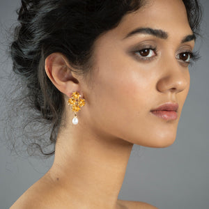 Close up of woman wearing gold Bloom earrings featuring four lotus flowers and a freshwater pearl 